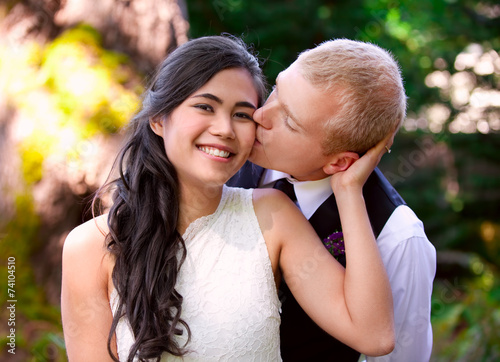 Caucasian groom lovingly kissing his biracial bride on cheek. Di