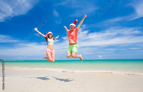 young couple in santa hats laughing on tropical beach. new year
