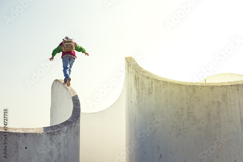 brave extreme man with backpack walking on a thin concrete wall