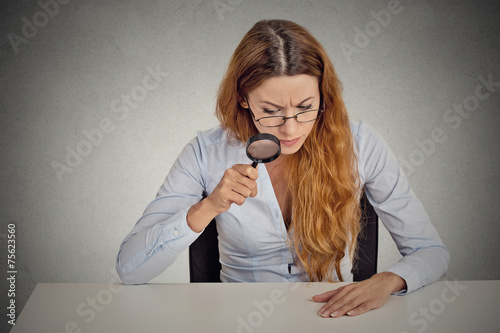 Woman skeptically looking through magnifying glass at table