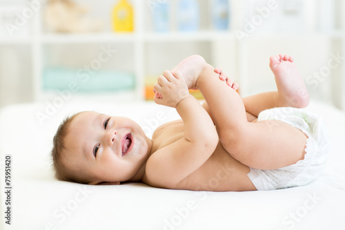 baby lying on white bed and holding legs