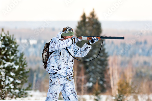 the hunter in winter camouflage shooting from a gun