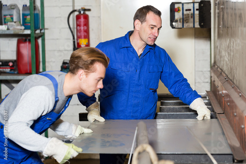 Two workers bending sheet metal with large machine