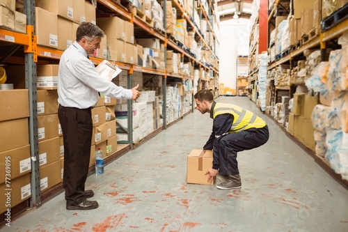 Manager watching worker carrying boxes