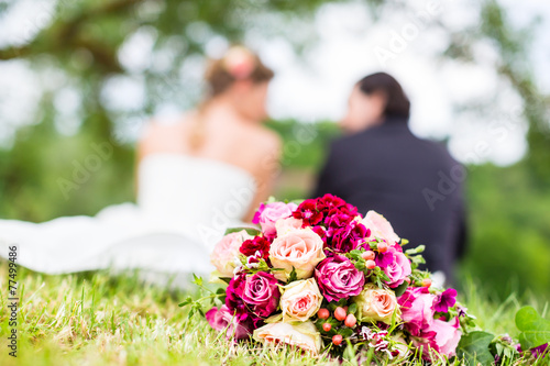 Hochzeitspaar mit Brautstrauß sitzt auf Wiese