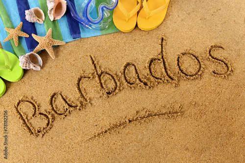 The word Barbados written in sand on a beach with towel flip flops seashells summer vacation holiday photo