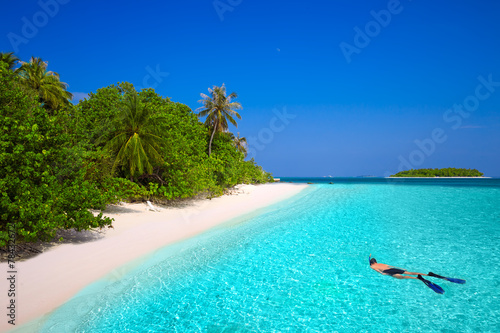 Young man snorkling in tropical island with sandy beach, palm tr