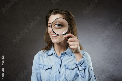 Cheerful woman looking through magnifying glass