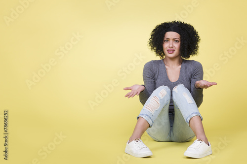 Young woman with questioning look isolated on yellow background.