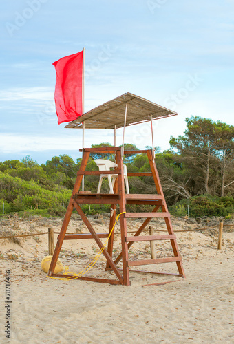 Empty lifeguard tower with red flag on the beach.