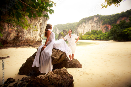 groom looks at bride sitting on rock at sand beach