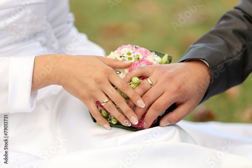 Dłonie młodej pary, obrączki i bukiet kwiatów.