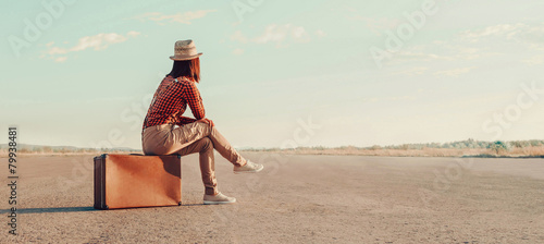 Traveler girl sitting on a suitcase on road