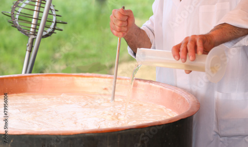 Cheesemaker pours milk rennet in copper pot for making cheese
