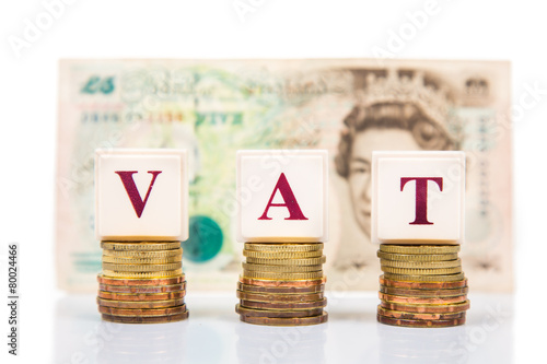 VAT concept with stack of coin and British Pound as backdrop