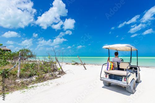 Young man driving on a golf cart at tropical white sandy beach