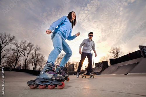 Girl on rollerblades and boy on skateboard in skate park