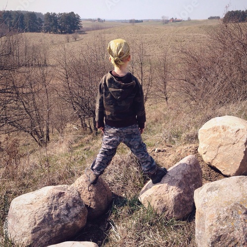 Chłopiec na wzgórzu stoi na kamieniach i patrzy w dal