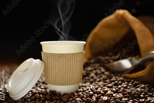 Paper cup of coffee with smoke and coffee beans on wooden table