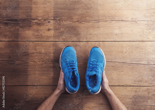 Man holding a pair of running shoes on a wooden floor background