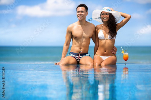 Asian young couple sitting in swimming pool under sunny summer