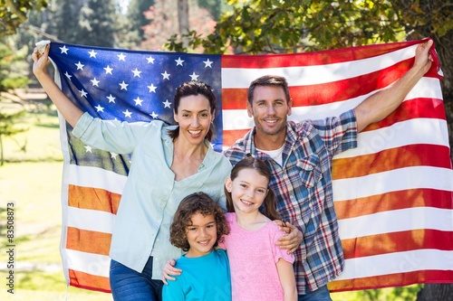 Happy family smiling with an american flag in a park