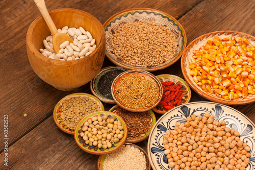 Various grain beans in small clay plates on natural textured woo