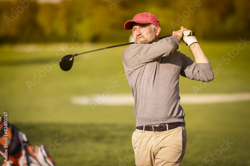 Male golf player teeing off with club.