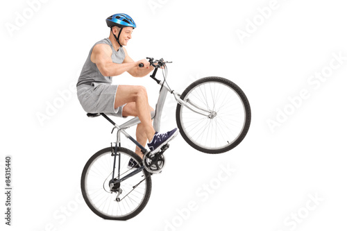 Joyful young biker doing a wheelie with his bicycle