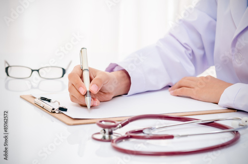 doctor writing record on folder on desk in office