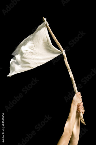 Hands holding white rag tied to a stick against a black background