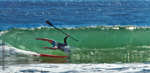 A paddleboarder loses his balance as he rides a big wave in to shore.