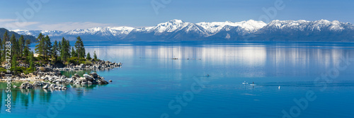 Paddle boarding calm Lake Tahoe with view on Sierra Nevada snowy mountains. 