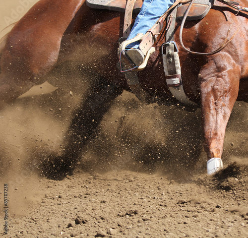 A close up action photo of a horse sliding around a barrel with dirt flying.