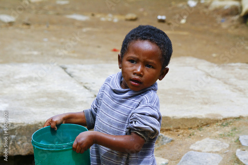 Poor malagasy boy carrying plastic water bucket - poverty