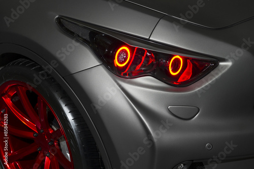 Predatory red car headlight and hood of powerful sports car with matte grey paint and wheel with red disc 