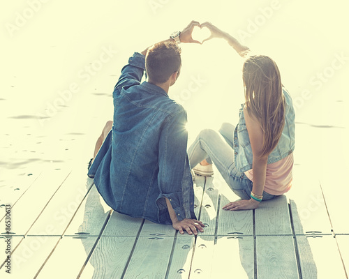 Couple in love sitting on the pier, their hands show heart