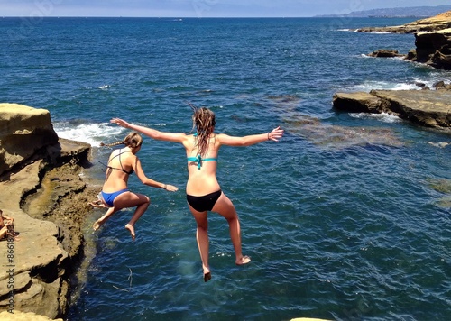  Two Young Daring Women jumping off cliff into ocean, San Diego, CA