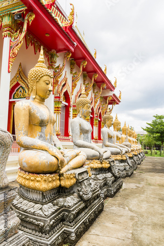 aged golden buddha in row beside temple