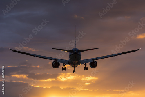 Plane is flying towards the runway. Cloudy orange sky.