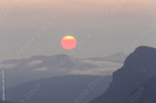 Huge red midnight sun above mountain range