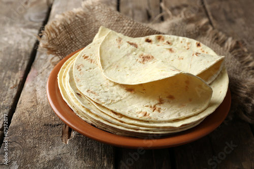 Stack of homemade whole wheat flour tortilla on plate, on wooden table background