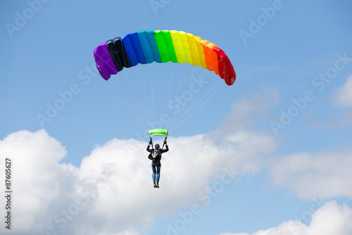 Parachutist on a bright parachute rainbow colors on bakcground blue sky with clouds