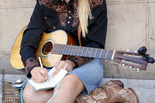 Momentos de inspiración. Chica rubia componiendo una canción sentada en el suelo de la calle. Joven músico con su guitarra. 