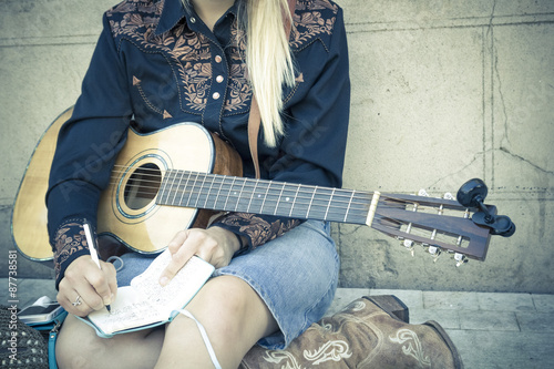 Momentos de inspiración. Chica rubia componiendo una canción sentada en el suelo de la calle. Joven músico con su guitarra. 