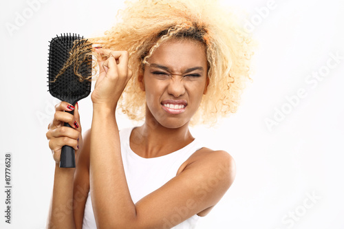  Splątane włosy. Ciemnoskóra młoda kobieta rozczesuje włosy szczotką