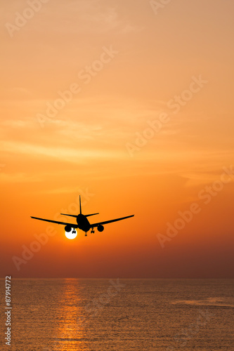 Silhouetted commercial airplane flying above the sea at sunset
