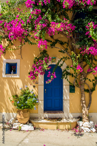 Traditional greek house with flowers in Assos, Kefalonia island, Greece.. Blue door and blue window surrounded by magenta flowers.