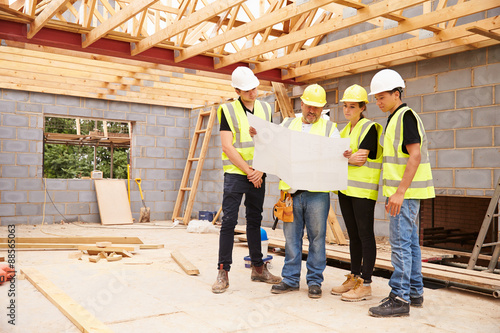 Builder On Building Site Looking At Plans With Apprentices