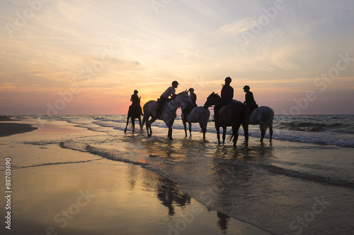 Jeźdźcy na koniach jadący brzegiem morza o zachodzie słońca